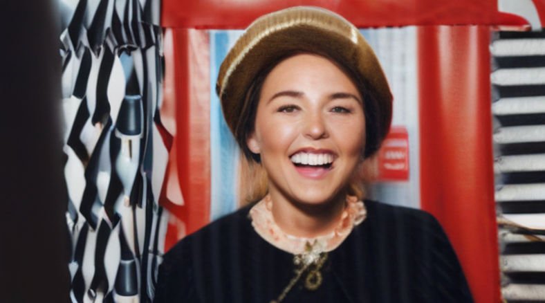 A woman wearing a news reporter attire smiling in front of a photobooth.